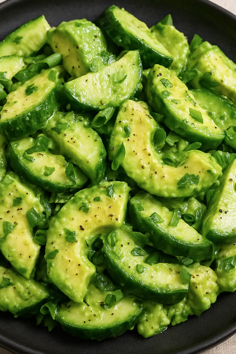 Healthy Avocado Cucumber Salad with green herbs served in a black bowl.