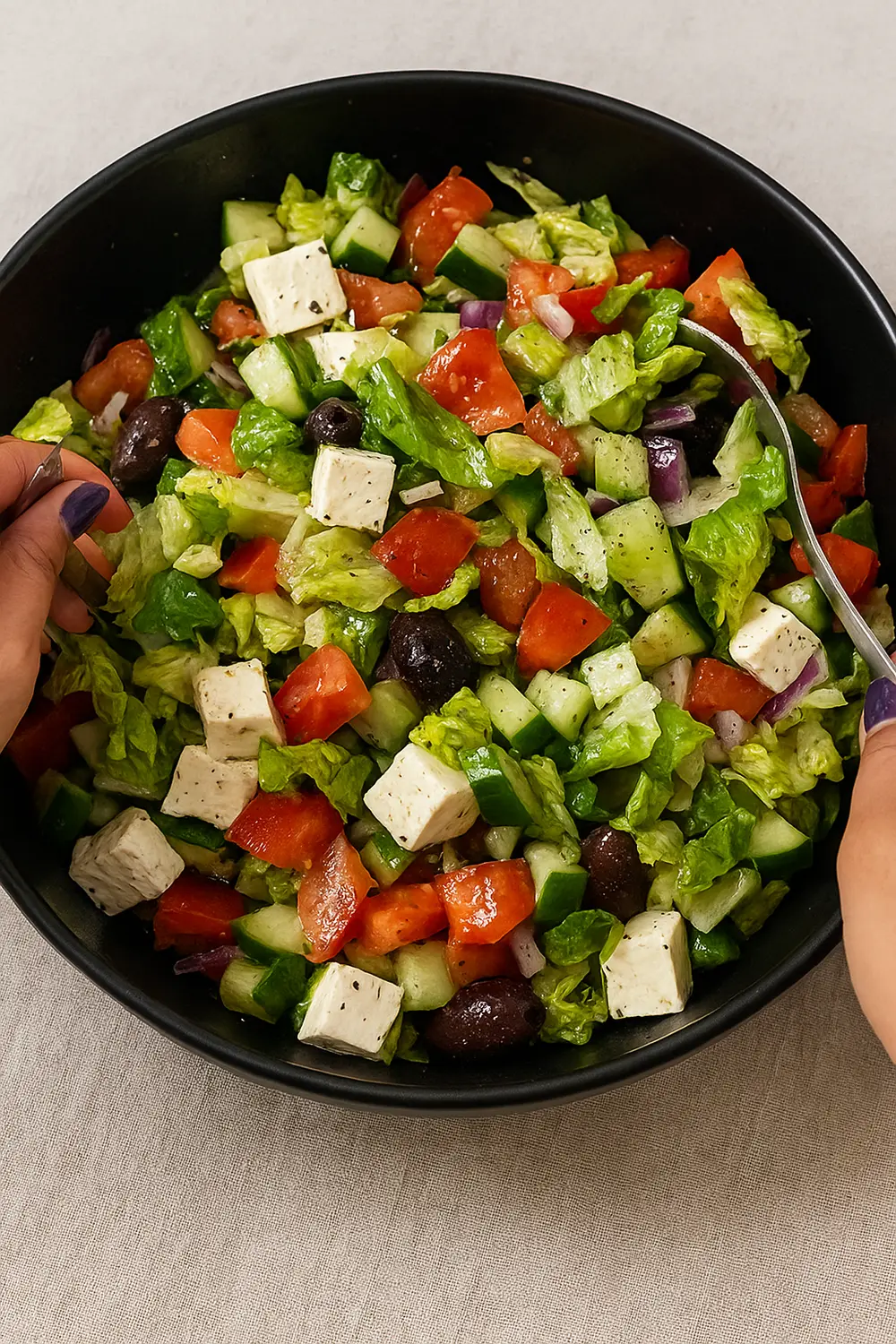 Greek tomato cucumber salad featuring fresh cucumbers, ripe tomatoes, feta cheese cubes, black olives, and romaine lettuce in a black serving bowl
